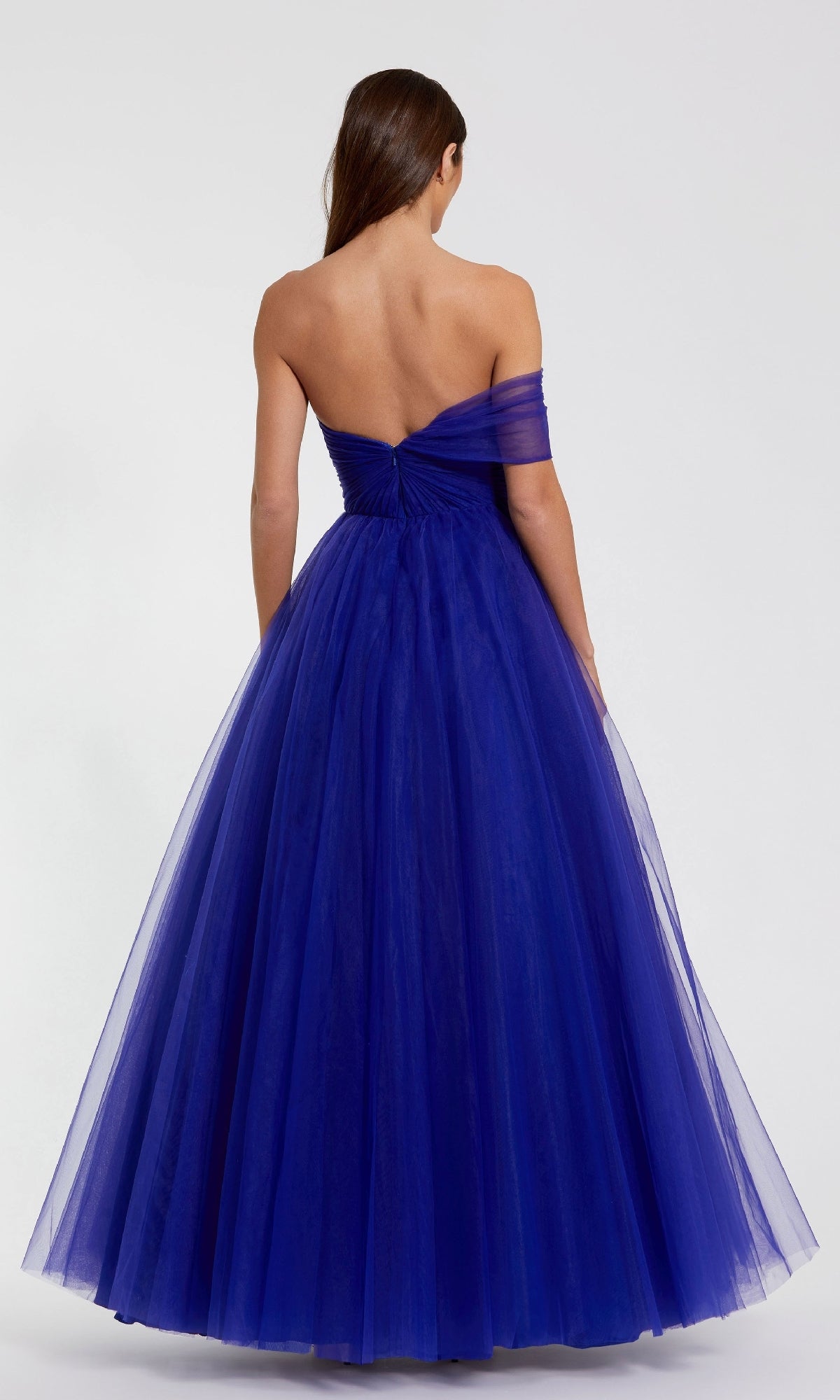 A woman is shown from the back against a plain light background, wearing a one-strap royal blue Mac Duggal 68713 long prom ball gown with tulle.